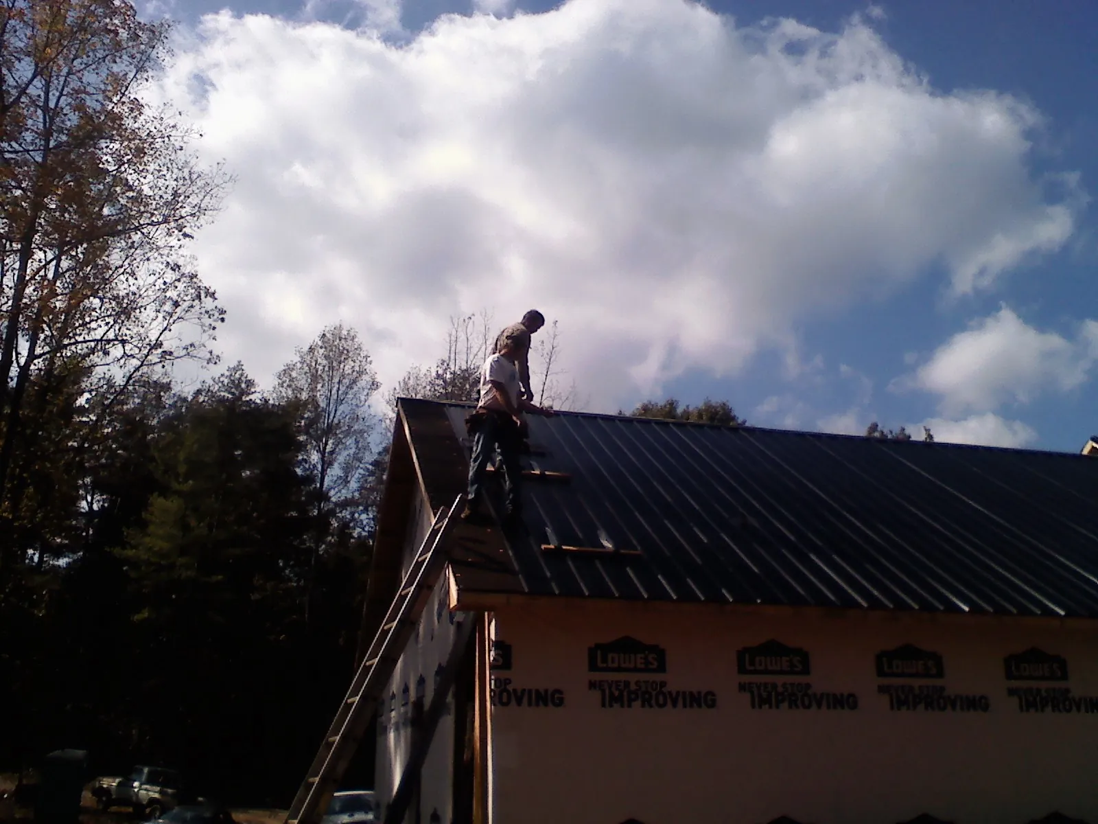 Roofer fastening dark metal panels high against a cloudy sky, from a Roof Inspection job in Atlanta
